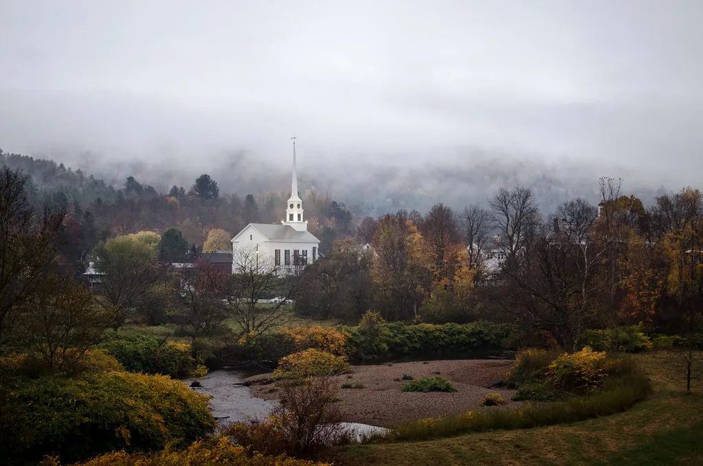 White church steeple rising over a misty fall valley near Stowe, Vermont