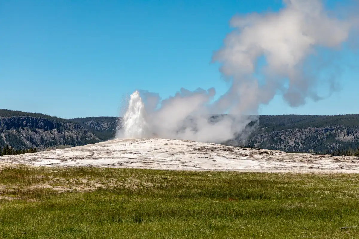 Old Faithful erupting with rainbow in steam